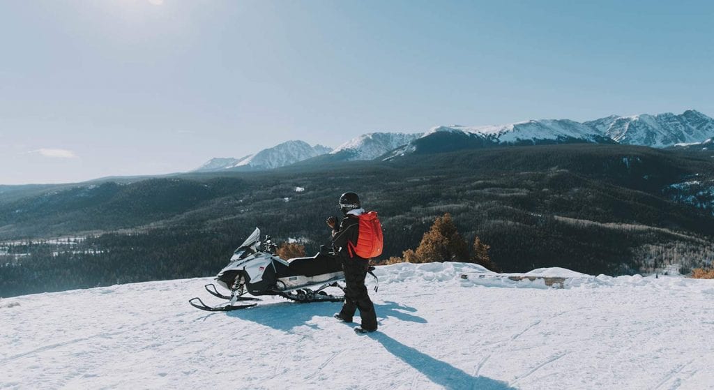 walking to a snowmobile in the mountains - APN Lodge