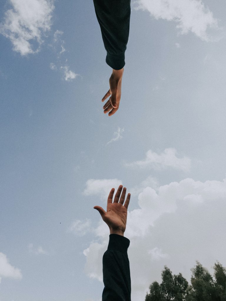 Two hands reaching towards each other across a background of the sky.