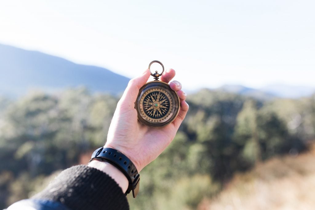 Someone holding an antique compass with a mountainous horizon in the background.