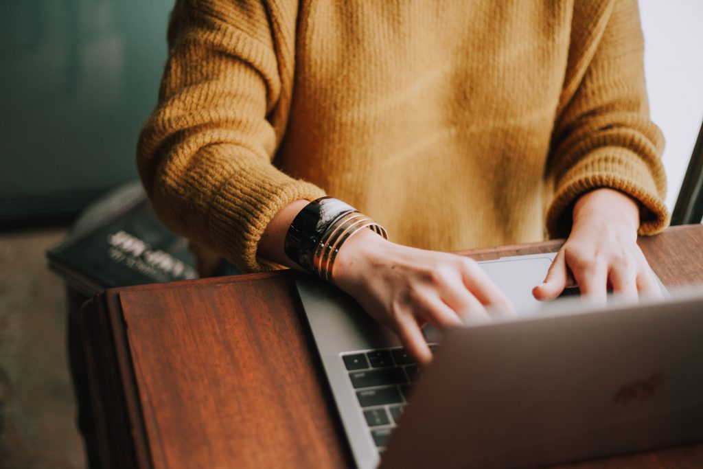 A woman in a mustard sweater researches on a silver laptop.