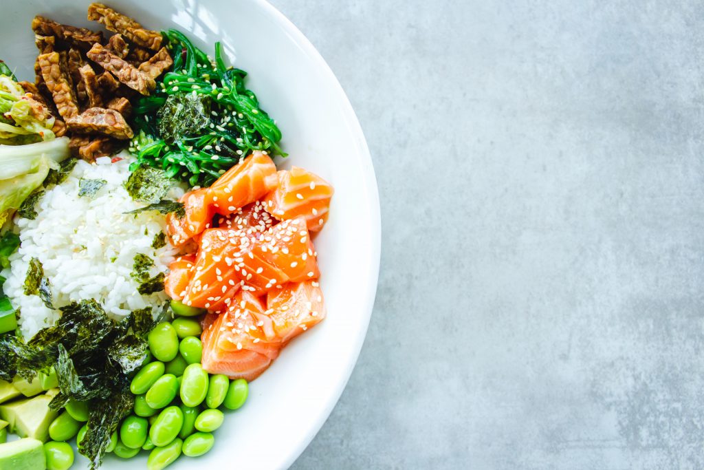 A white bowl full of healthy food: salmon, edamame, seaweed, rice, avocado, seeds, and more.