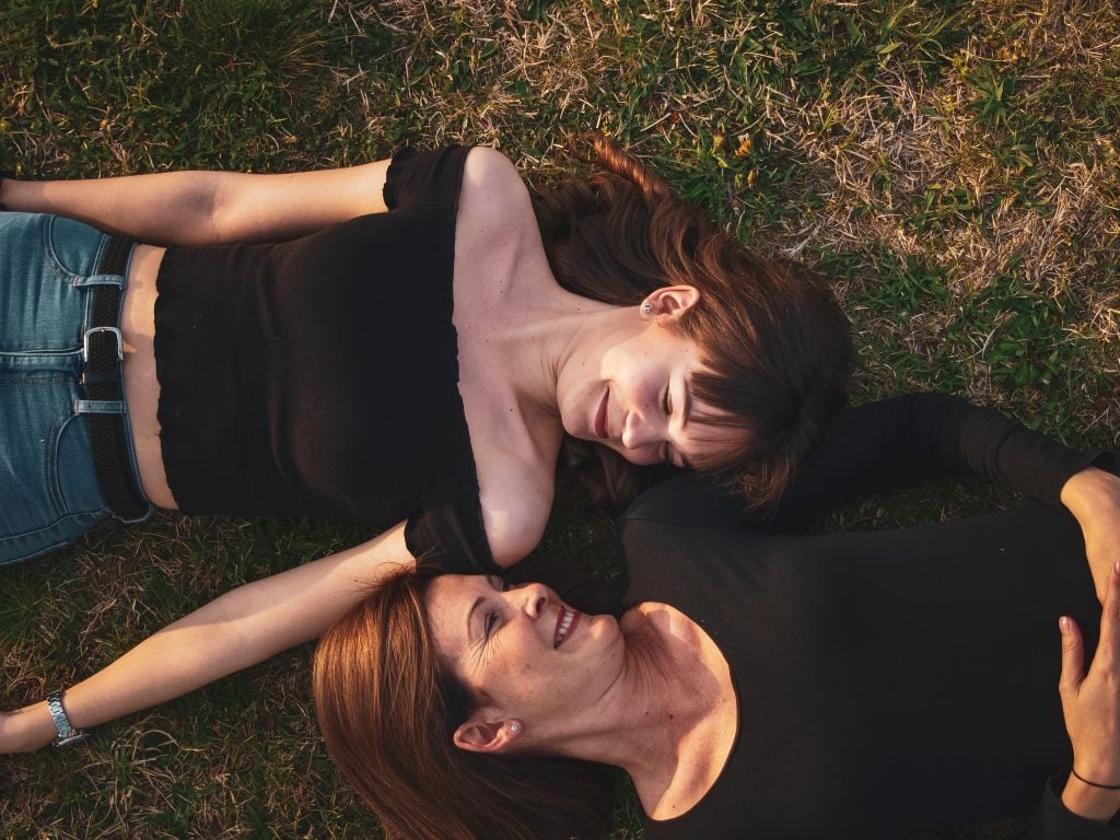 A mother and daughter laying on the ground, smiling at each other.