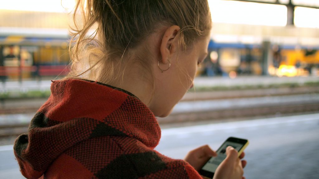 A woman checks in on an app on her phone as she waits for the train.