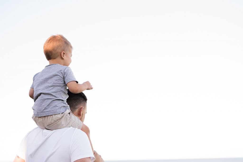 A father carries his toddler son on his shoulder.