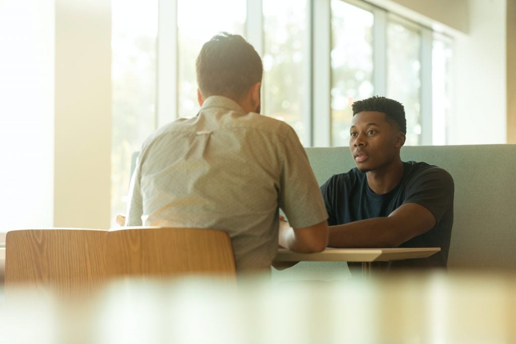 Two men sitting at a booth having a conversation.