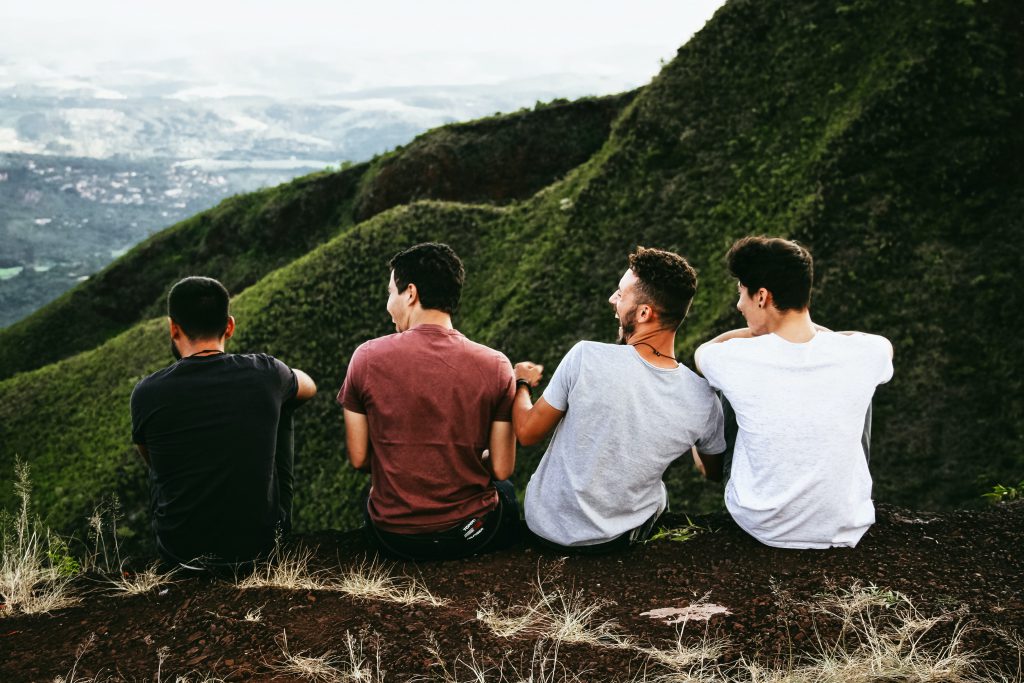 Four men sitting on the side of a lush mountain.