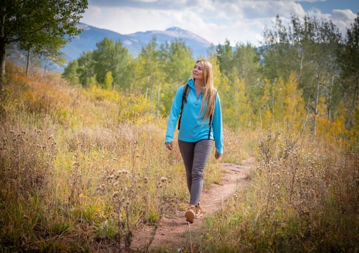 A woman in a blue jacket hikes through a trail in Colorado.