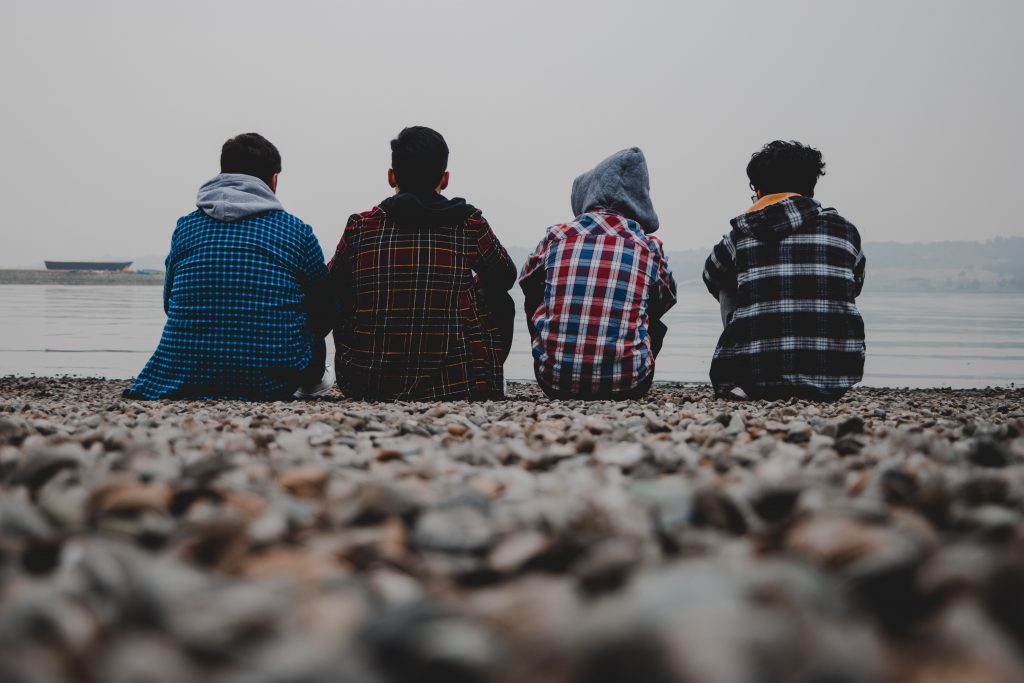 Four kids hanging out on a rocky beach, all wearing flannels.