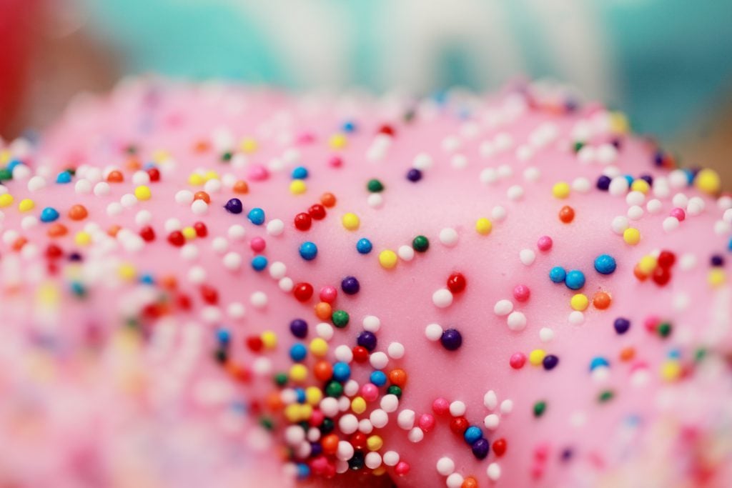 Close up of a donut topped with pink frosting and rainbow sprinkles.