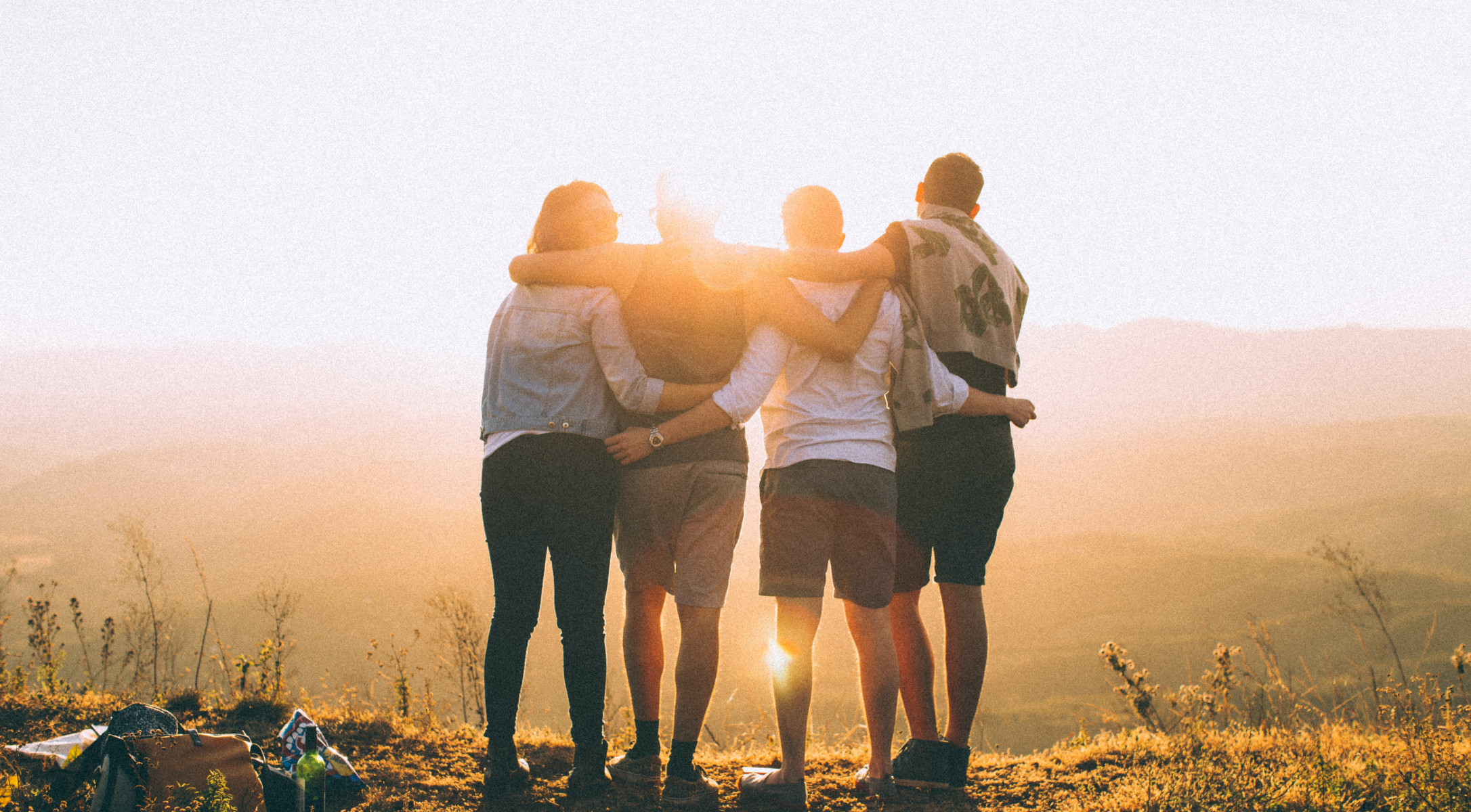 Four friends gathered on a mountaintop watching the sun set.