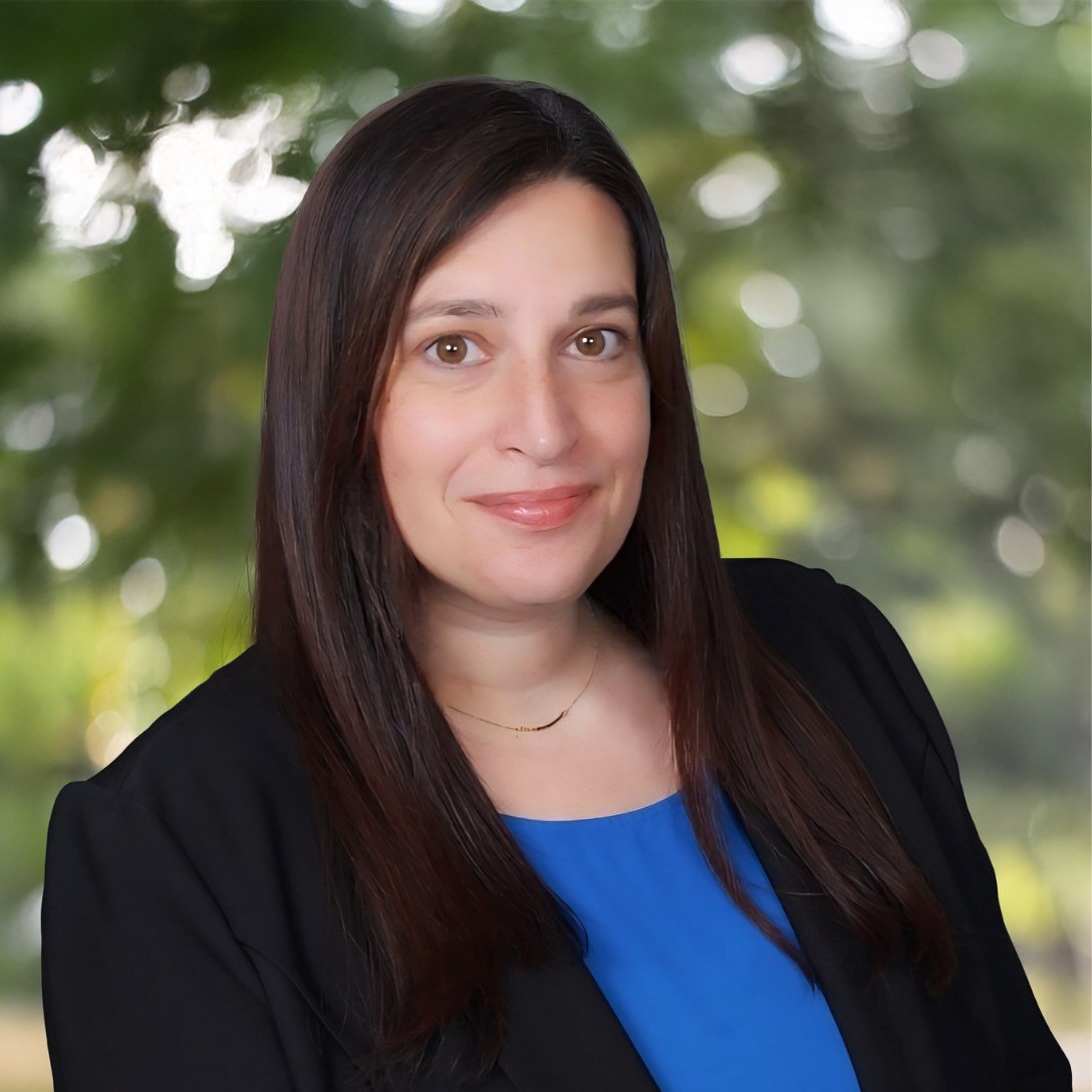 Headshot of Karri Francisco wearing a black blazer with a blue shirt in front of a blurred greenery scene.