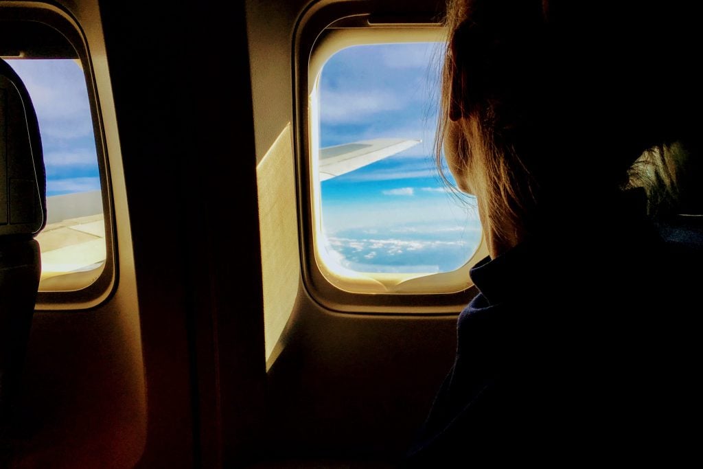 A woman looks out the airplane window to crystal blue waters.