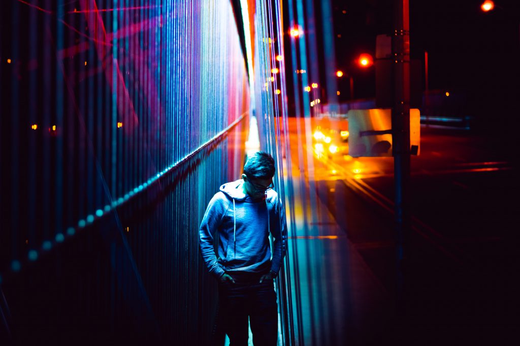 A man bathed in neon lights on a street corner.