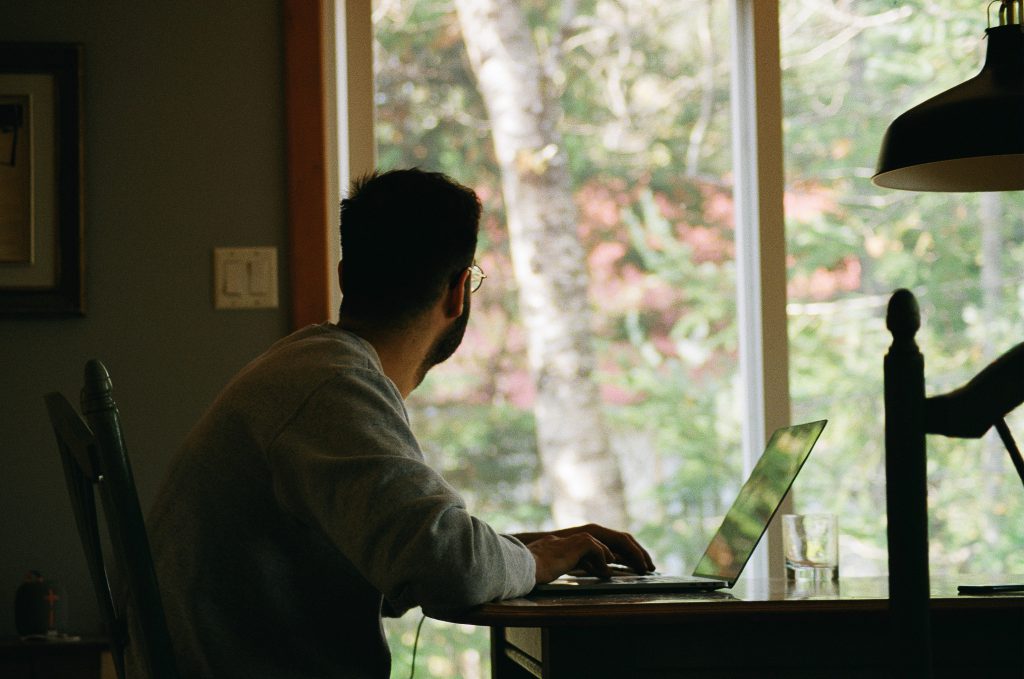 A man sits inside looking out the window during COVID isolation.