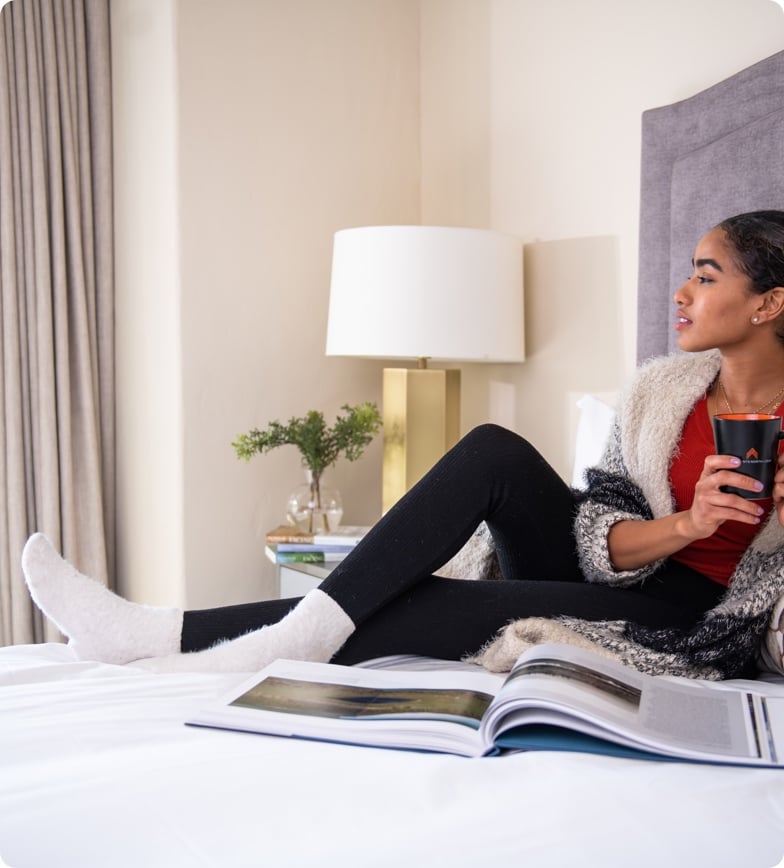 Woman sitting on bed with coffee and magazine