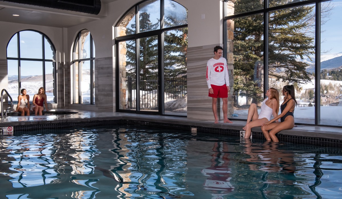 Two people talking to a lifeguard aside the APN pool, and two people sitting next to the hot tub