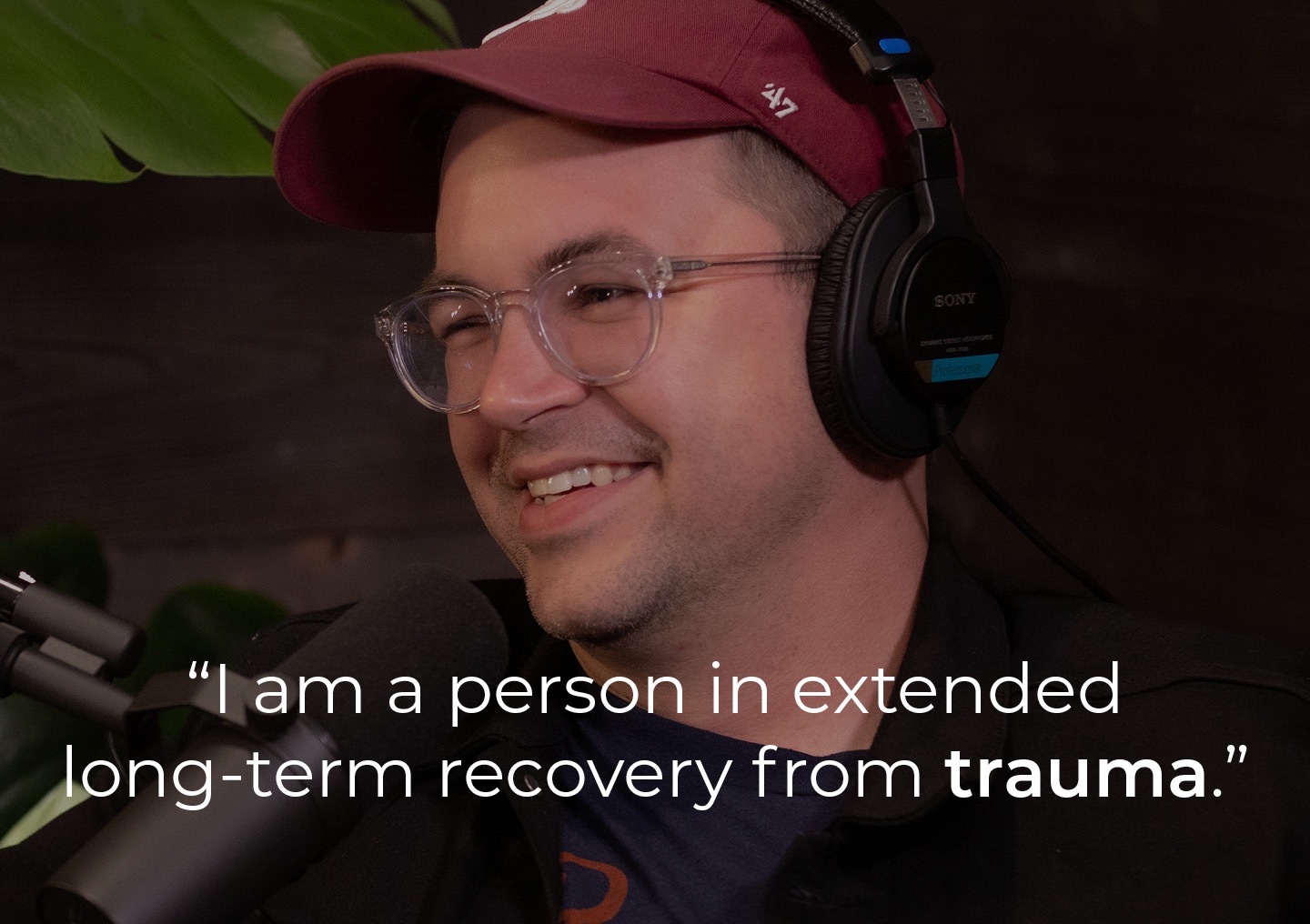 Elliott speaking into a podcast microphone with a text overlay: I am a person in extended long-term recovery from trauma.