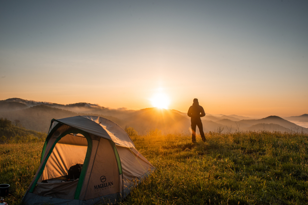 A camper greets the sunrise outside of his tent.