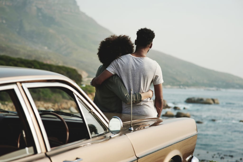 A couple sits on the hood of their car overlooking the ocean.