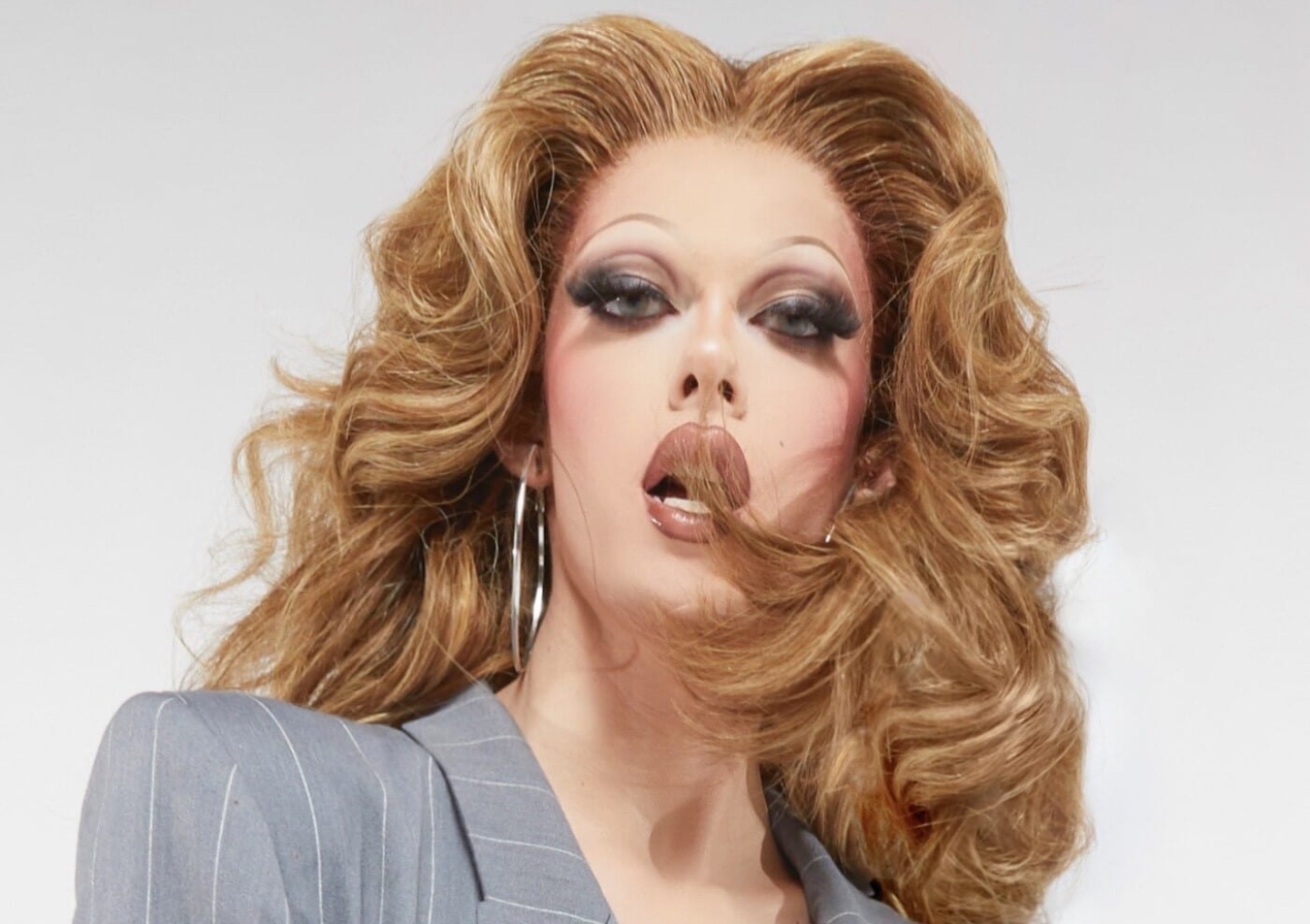 Gigi Goode poses in full glam in a fitted gray suit.