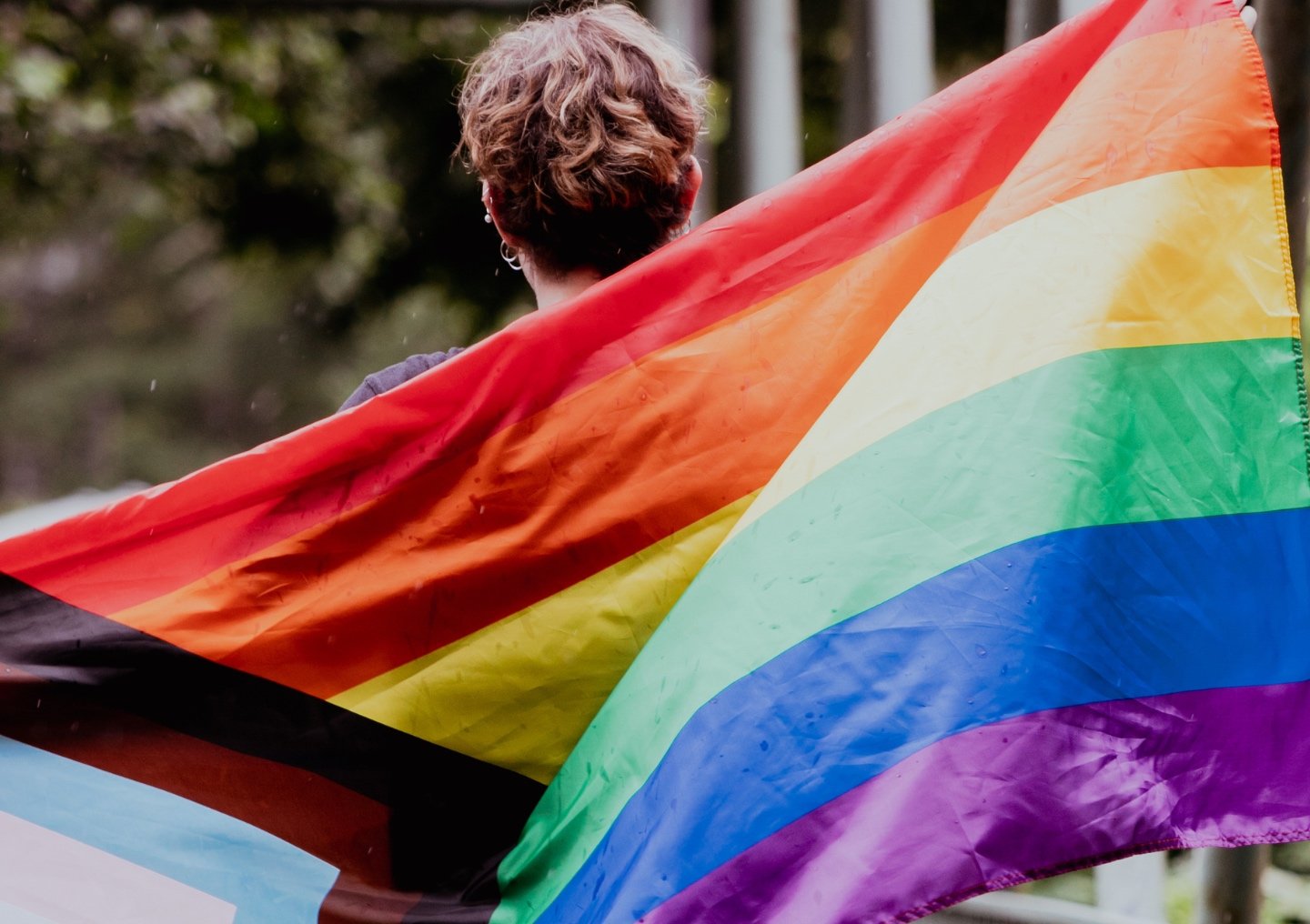 A person marches with an inclusive pride flag flowing behind them.