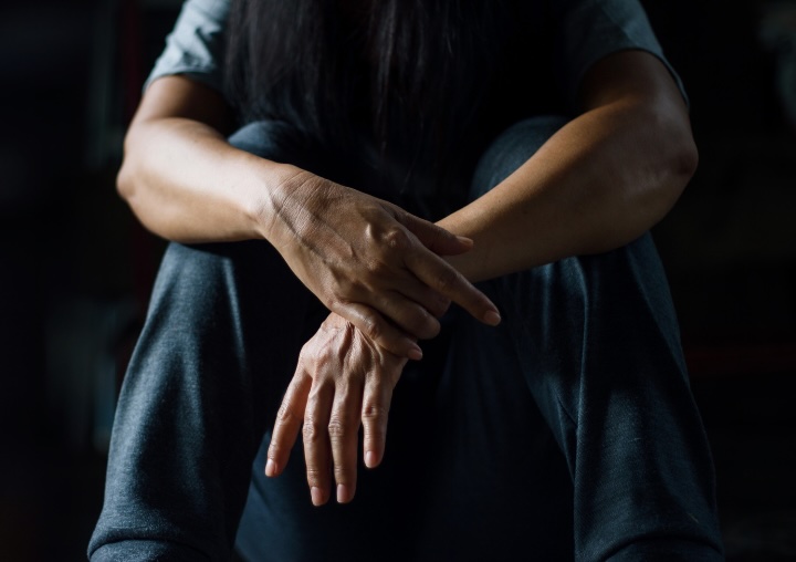 A person sitting on the ground in a dark room with their hands crossed.