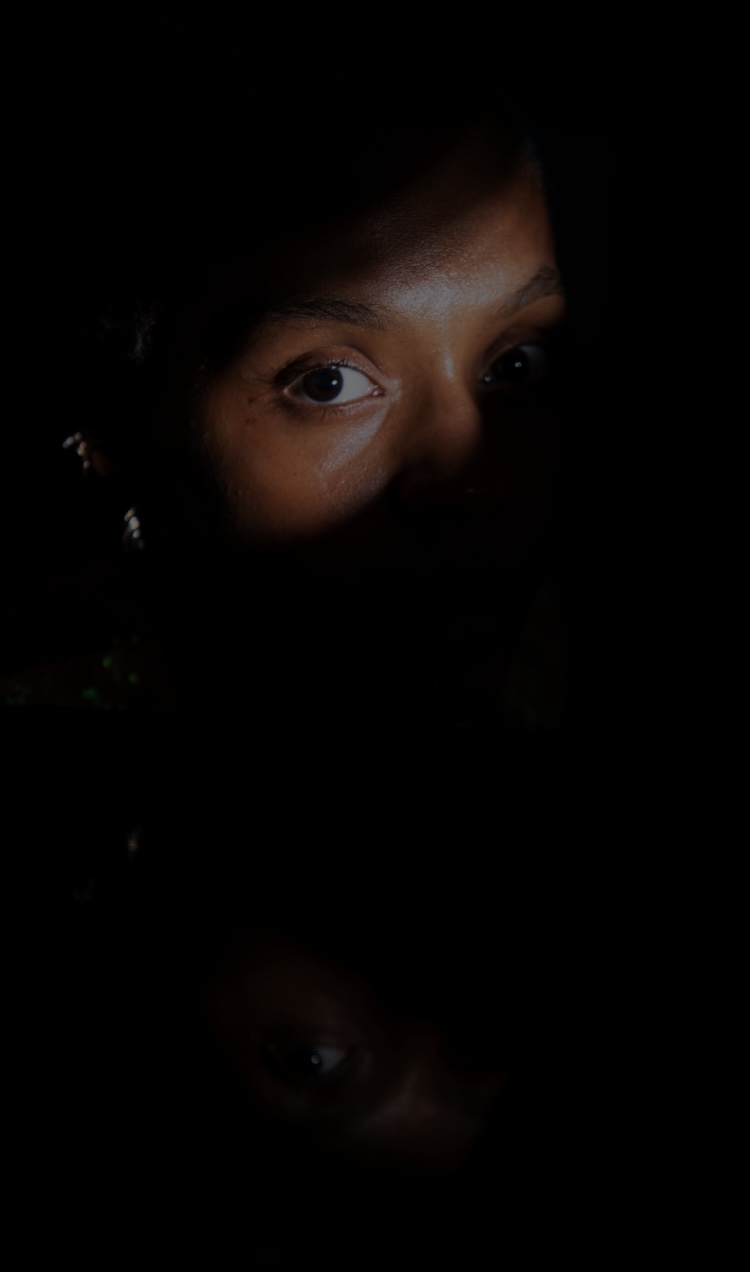 Someone sits in the dark with a beam of light across one eye.