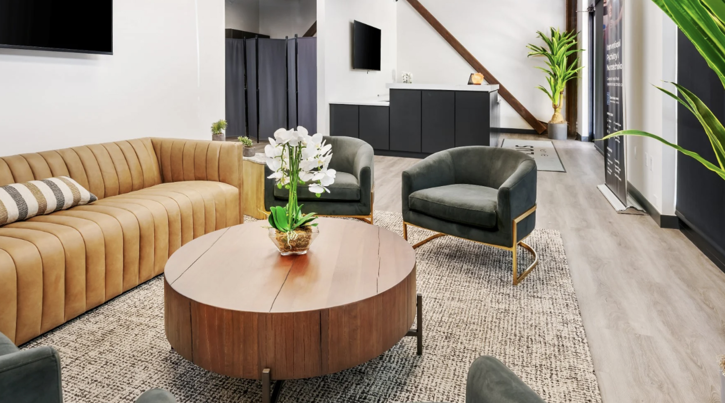 Modern office lobby with a tan sectional sofa, two green armchairs, a round wooden coffee table with an orchid centerpiece, and a welcoming atmosphere, reflecting the supportive environment of the Intensive Outpatient Program for mental health recovery in Boulder, CO.
