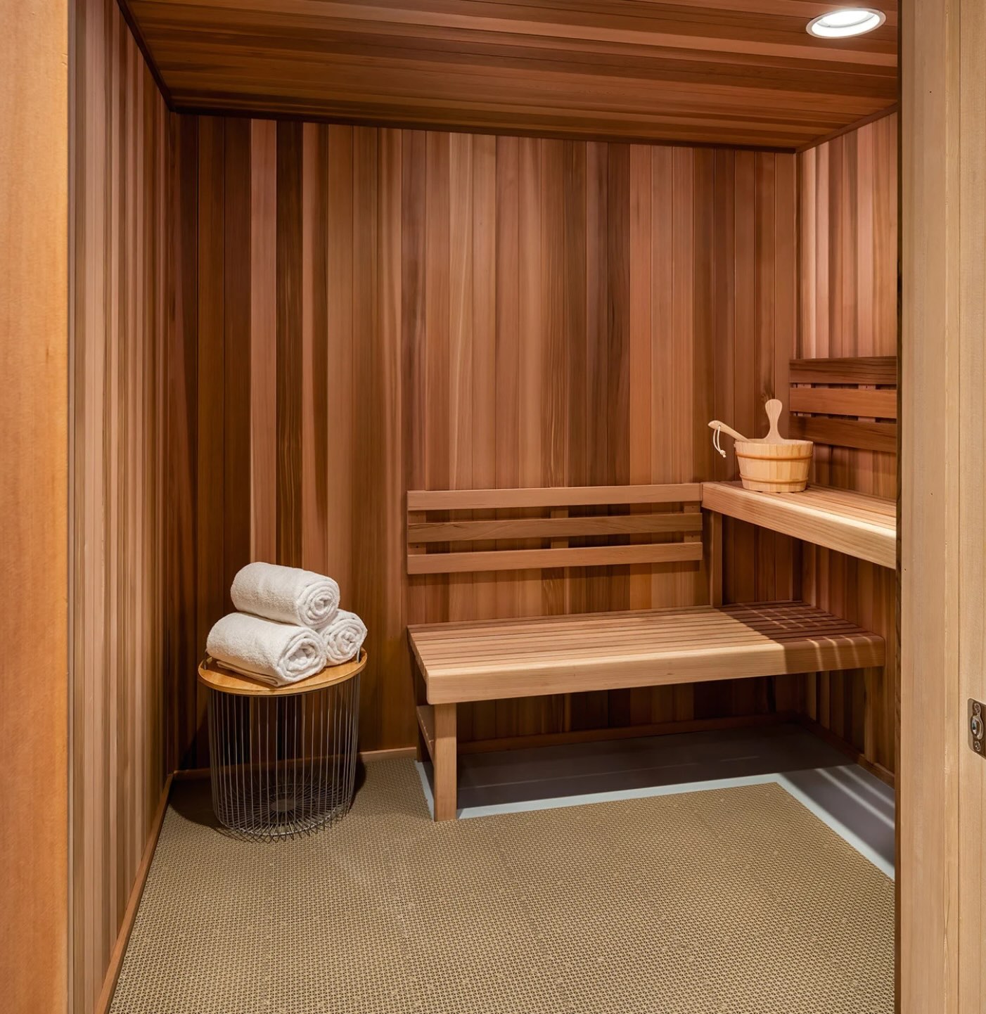 The sauna at APN Dallas-Fort Worth: a wooden sauna with plush folded towels, a bench, and sauna supplies on a shelf.