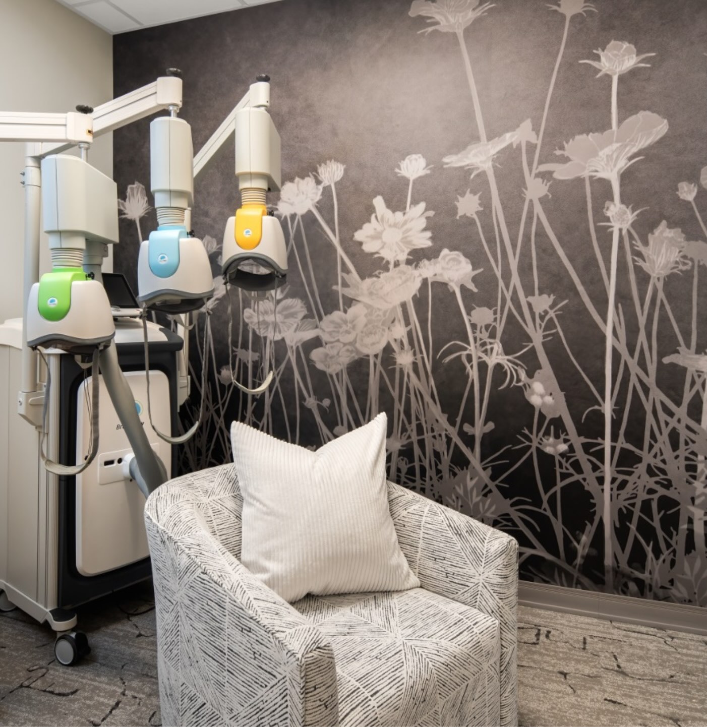 The Deep TMS room at APN Dallas-Fort Worth: a deep TMS machine with a comfortable chair against a wall with a flower mural.