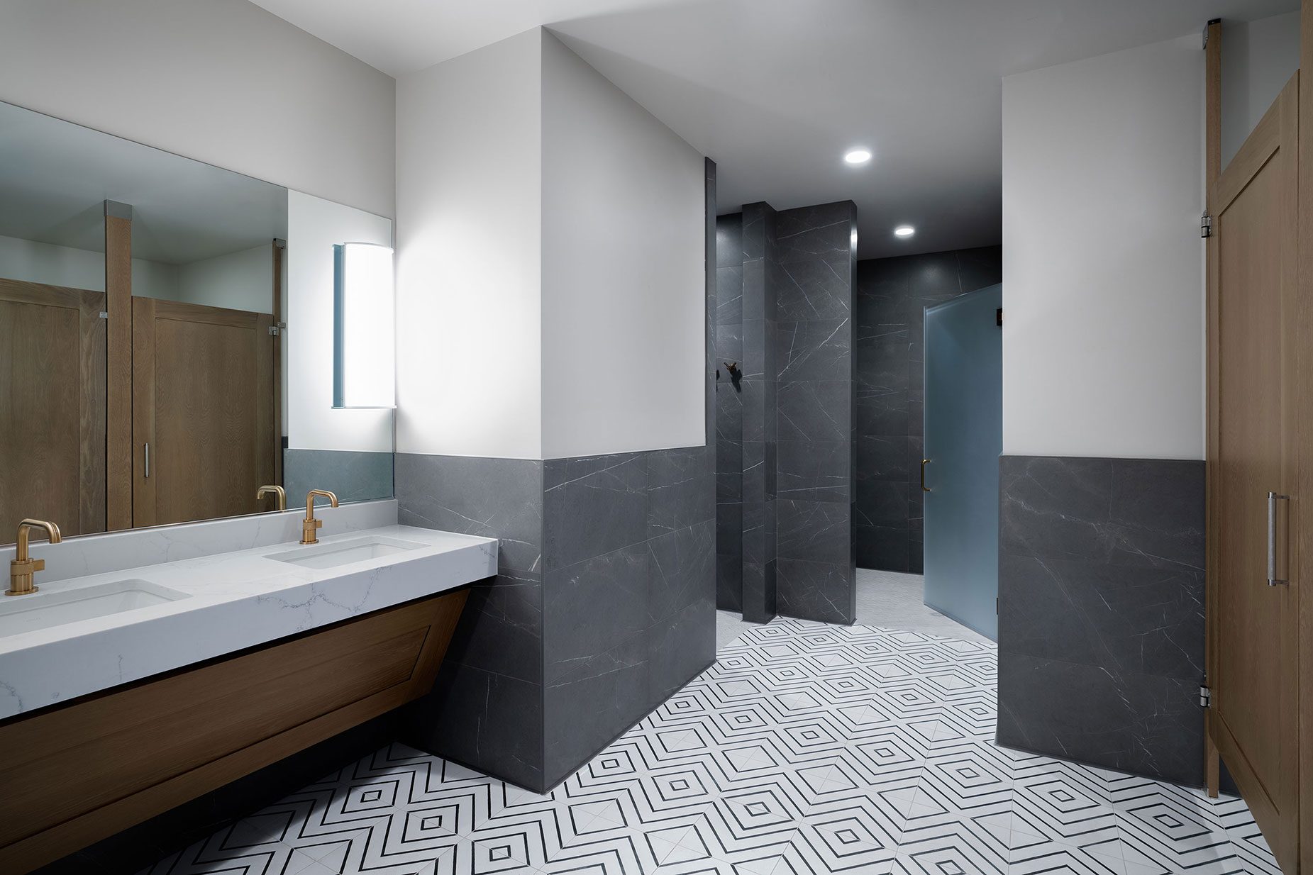 Luxury bathroom interior featuring modern design elements, including a marble sink with gold faucets, geometric patterned flooring, and sleek dark stone walls, reflecting the upscale amenities at All Points North Denver treatment center.