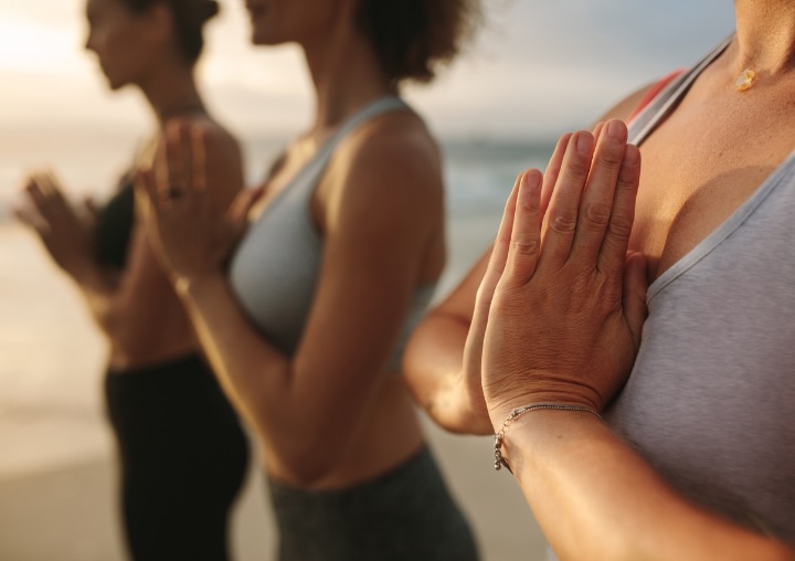 Women stand on the beach during sunrise while meditating.
