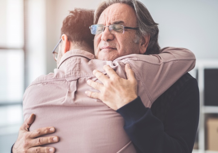 Two men embrace platonically in a moment of vulnerability.