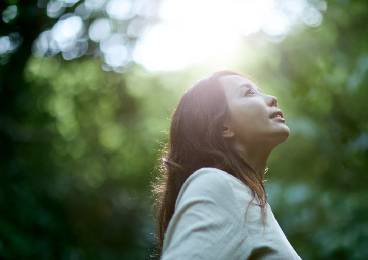 A woman stands in a lush green forest, looking hopeful.