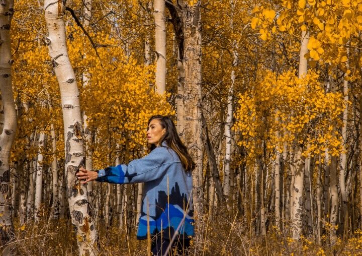 A woman walks between Aspen trees, retracing her steps.