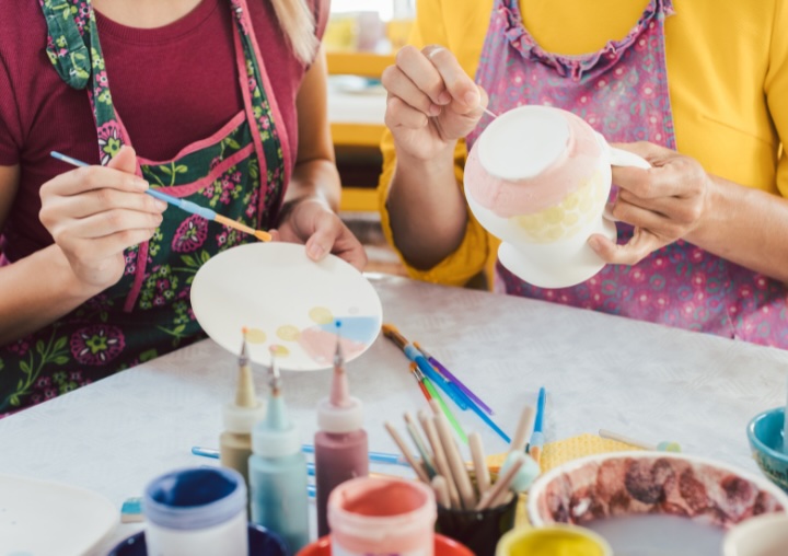 Two women wear colorful aprons while painting pottery at Painting with a Twist.