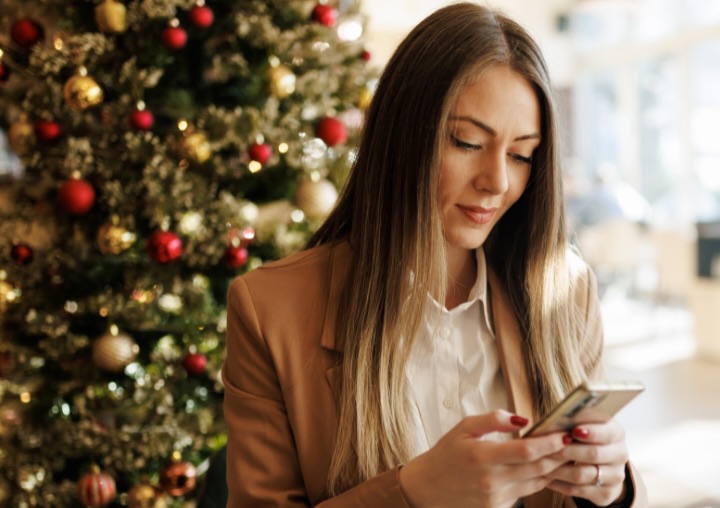A woman pauses to read holiday support resources on her phone while at a cafe during the holiday season.